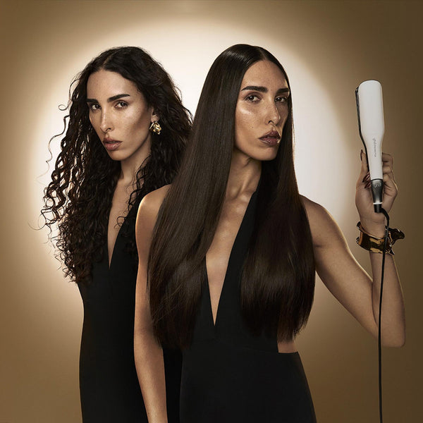 Two women with long hair, one holding a hair straightener against a brown background