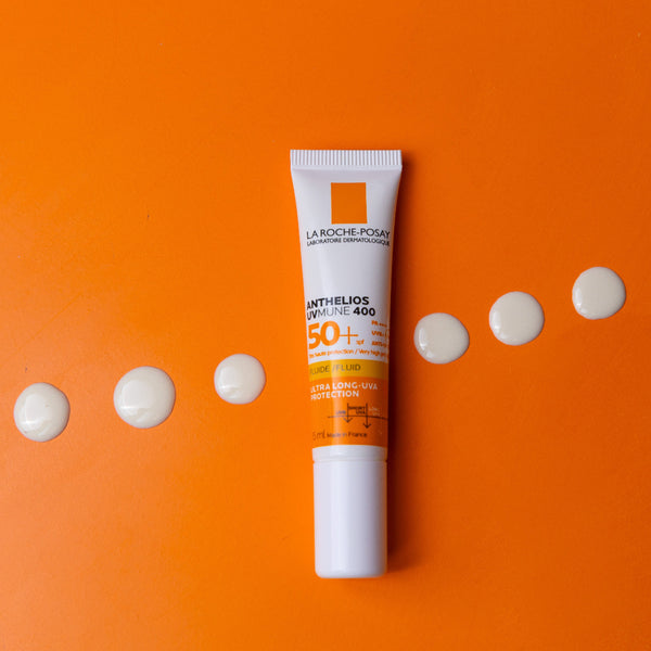 La Roche-Posay sunscreen tube on an orange background with white dots.