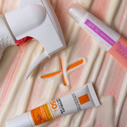 Two sunscreen tubes and a white device on a textured pink surface
