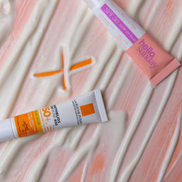 Two sunscreen tubes on a textured pink surface
