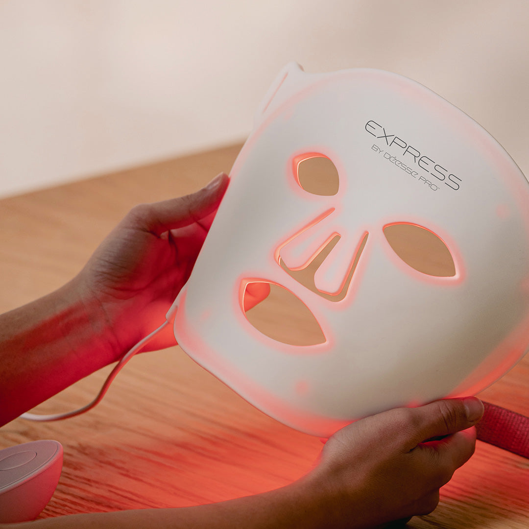 Person holding a white LED face mask with red light on a wooden surface