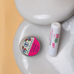 Small container and tube on a white ceramic dish with a pink background