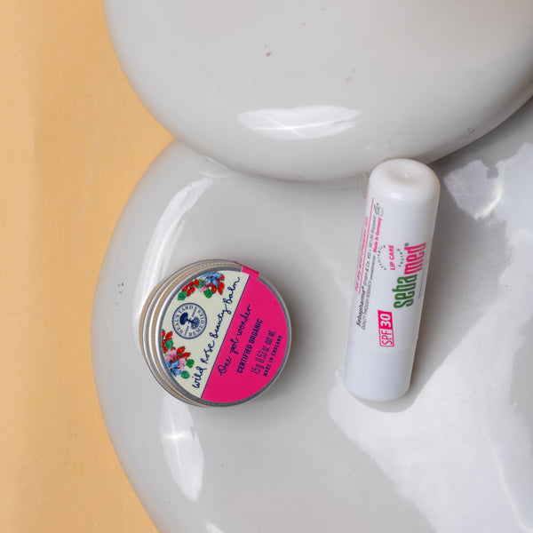 Small container and tube on a white ceramic dish with a pink background