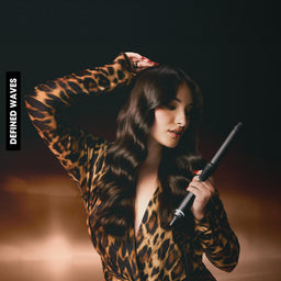 Person in leopard print outfit holding hair curlers against a dark background