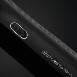 Close-up of a black device with 'ghd chronos curve' branding on a dark background