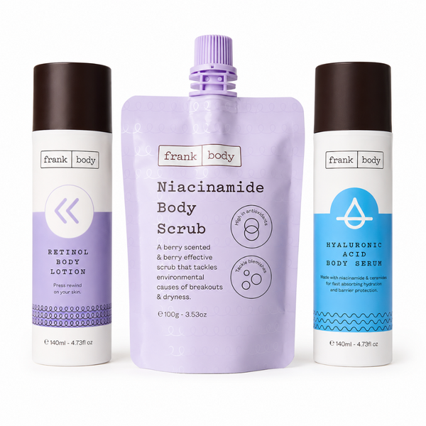 Three Frank Body skincare products on a white background: a lavender body scrub squeeze pouch in the center, flanked by a retinol body lotion bottle on the left and a hyaluronic acid body serum bottle on the right.