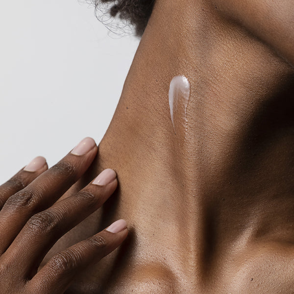 Close-up of a hand applying cream to a shoulder with a neutral background