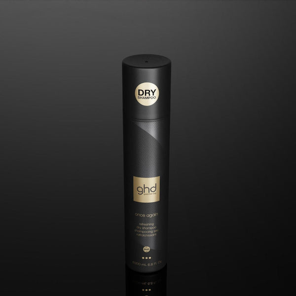 A single black cylindrical hair product container with gold and white branding, standing upright on a dark reflective surface against a black background.