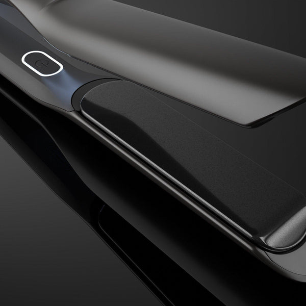 A close-up studio shot of a sleek black hair straightener with glossy metallic edges, shown open against a dark reflective background.