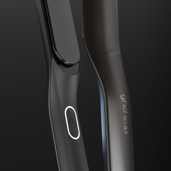 Close-up of a sleek dark gray hair straightener with a glossy black paddle and a white oval logo, set against a dark gradient background. The brand name 'sophie' is visible on the handle.