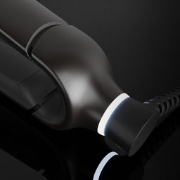 A close-up of a glossy black hair styling tool, likely a flat iron or curling iron, showing the heating plate and cord connector against a dark background.