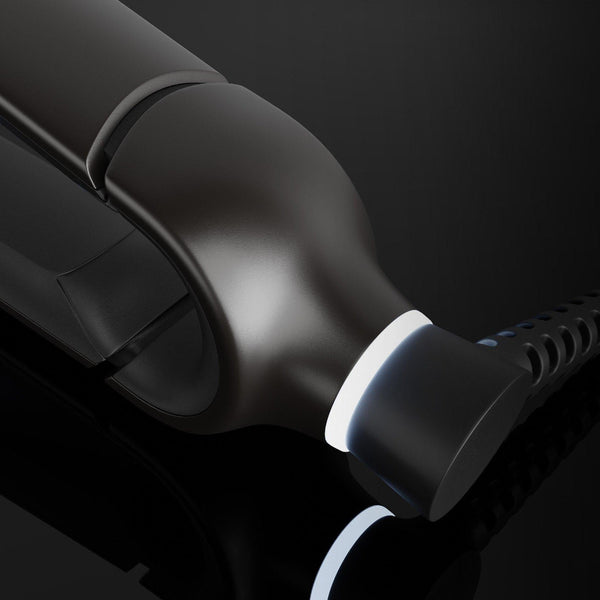 A close-up of a glossy black hair styling tool, likely a flat iron or curling iron, showing the heating plate and cord connector against a dark background.