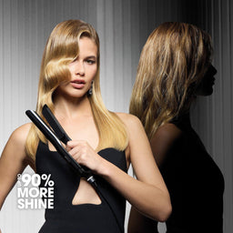 A blonde woman in a black dress holds a black hair straightener, with her reflection visible against a dark gray paneled background. Text in the lower left reads '#99 MORE SHINE'.