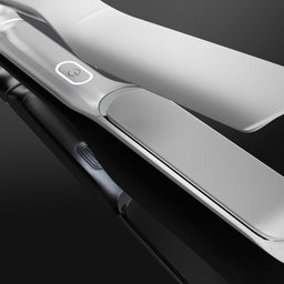 A close-up studio shot of a sleek silver hair straightener with its plates partially open, set against a dark reflective background.
