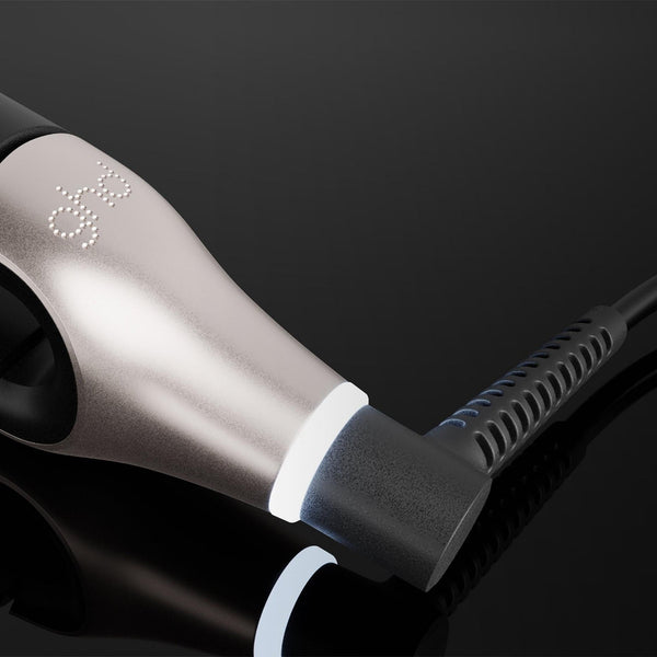 A close-up of a black and silver hair straightener plugged into a black power cord against a dark reflective background.