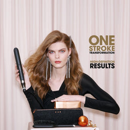 A woman with long wavy light brown hair models a black hair straightener, holding it up to her hair. She is wearing a black long-sleeve top and dangling silver earrings, standing in front of a light beige curtain backdrop.