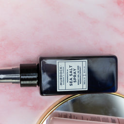 Black spray bottle labeled 'Hurdock' on a pink background