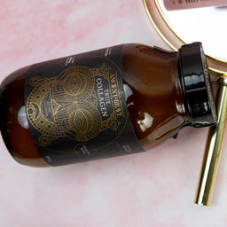 Brown bottle with gold label on a pink surface, next to a white tube of skincare product.