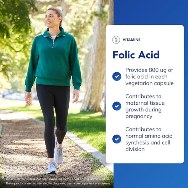A woman in a green quarter-zip pullover and black leggings walks on a park path next to a large informational graphic about folic acid vitamins.