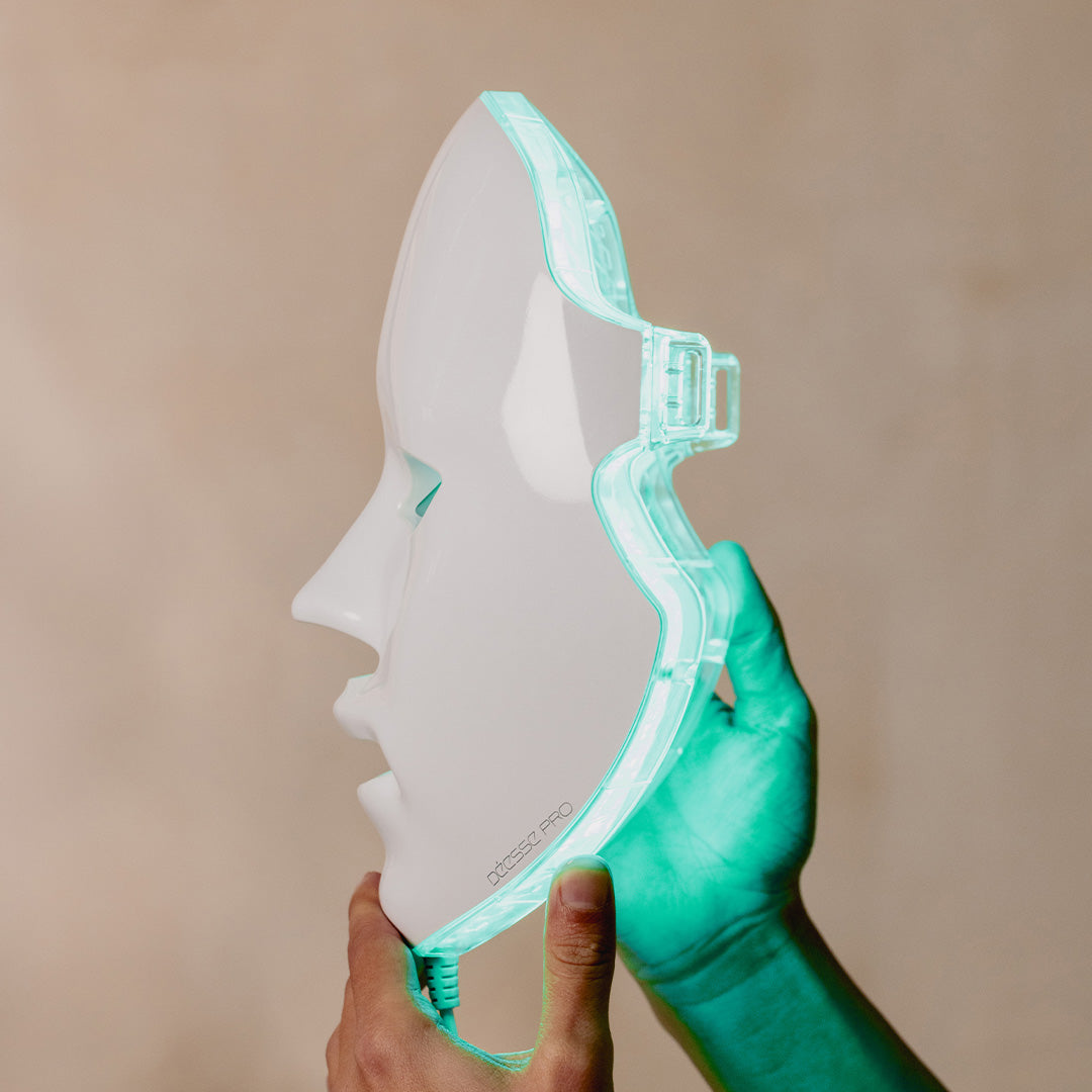 Hand holding a face-shaped mask with a green border against a beige background
