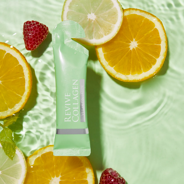 Revive Collagen Vegan 28 Days tube in a pool of water with slices of orange and raspberries 