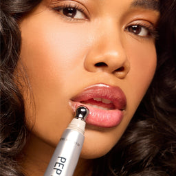 Close-up of a woman applying a lip product from a silver tube labeled 'PEPTI...' to her lower lip.
