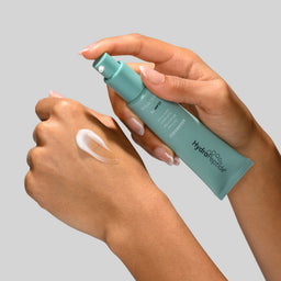 Person applying a green skincare product to their hand on a gray background