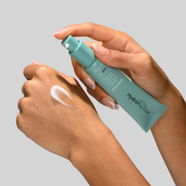 Person applying a green skincare product to their hand on a gray background
