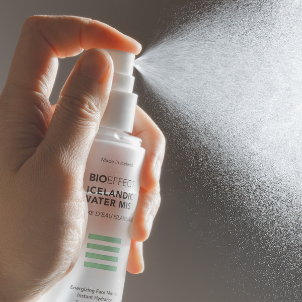 Hand holding a Bioeffect spray bottle with mist being released against a dark background