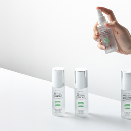 Hand holding a skincare product with other skincare bottles on a white background