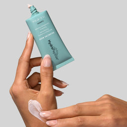 Hand applying a skincare product from a tube labeled 'hydropeel' on a gray background