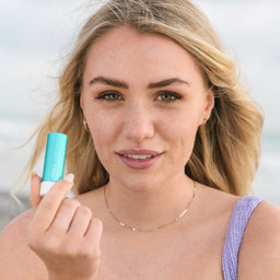 Model holding COOLA Classic Liplux SPF30 Original to her face