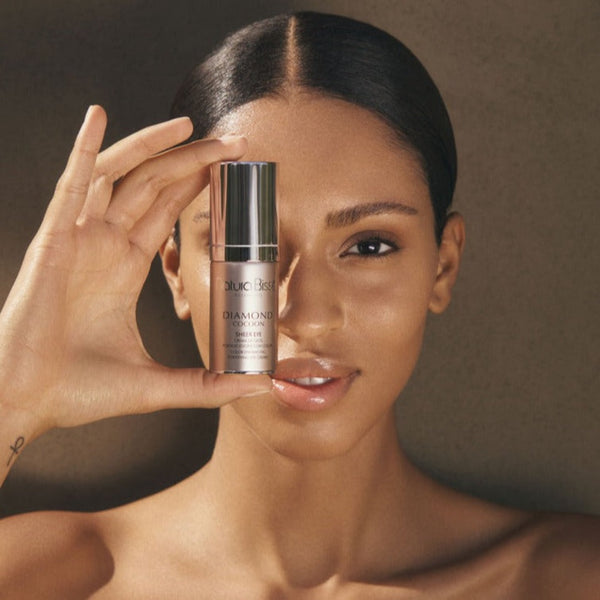 a bottle of Natura Bisse Diamond Cocoon Sheer Eye held to a models face