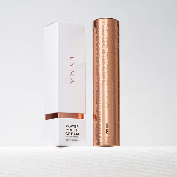 LYMA Power Youth Cream 120ml tube in a hammered rose gold finish, standing next to its white and rose gold outer packaging box on a light gray background.