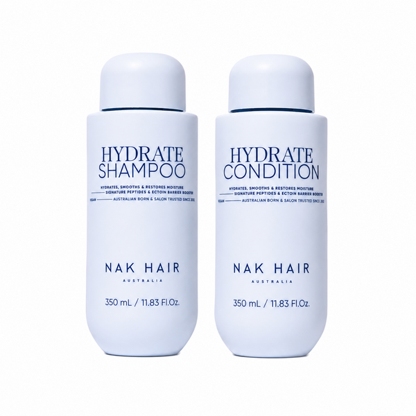 Two white cylindrical bottles of NAK Hair hair care products on a plain white background. The left bottle is labeled 'HYDRATE SHAMPOO' and the right bottle is labeled 'HYDRATE CONDITION'.