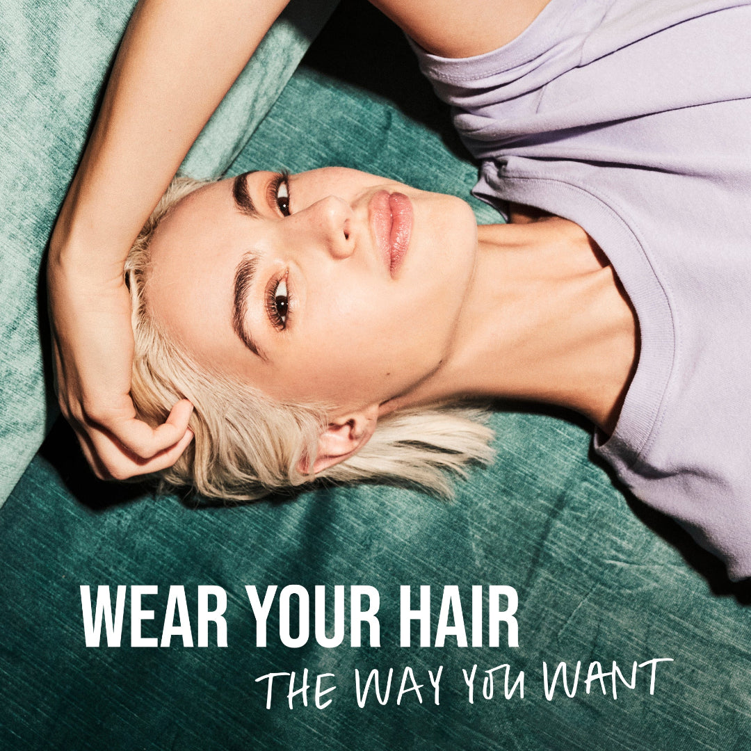 Person with short blonde hair lying on a green surface with text 'Wear Your Hair The Way You Want'.