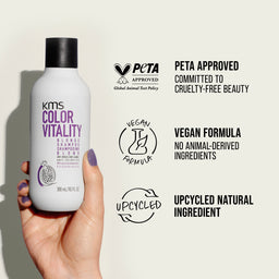KMS Color Vitality shampoo bottle held by a hand with PETA approval and vegan formula labels on a light background.