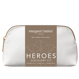 A white pebbled leather cosmetic pouch with a gold zipper, featuring a brown paper label that reads 'Margaret Dabbs London Heroes Discovery Kit'.