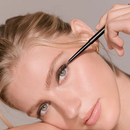 Woman applying eyeliner with a brush on a neutral background