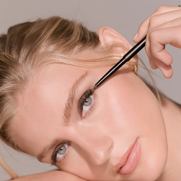 Woman applying eyeliner with a brush on a neutral background