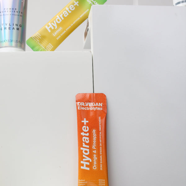 Orange 'Hydrate+' supplement stick pack on a white surface with other supplement packages in the background.