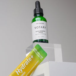 Votary serum bottle and Hydrate+ lemon drink package on a gray background