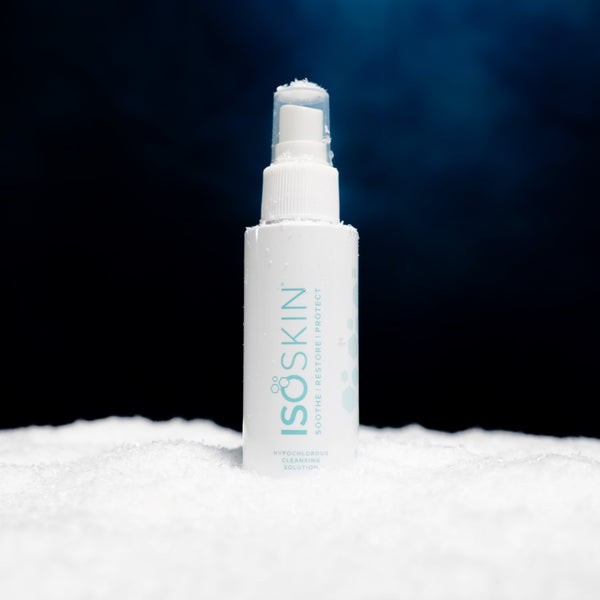 A white spray bottle of Dr. ISOSKIN Soothing Barrier Protect Hydrochloric Acid Cleansing Solution, standing upright in a bed of white snow against a dark blue and black background.