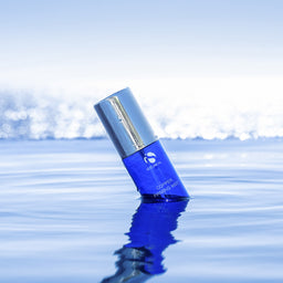 Blue cosmetic bottle with silver cap on a reflective water surface