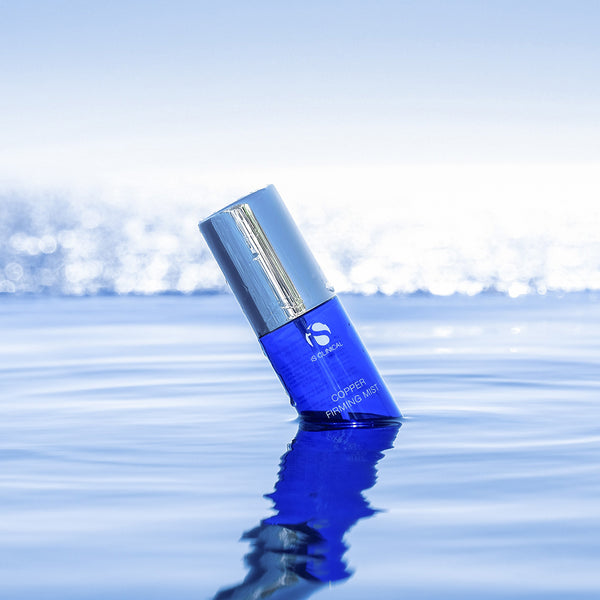 Blue cosmetic bottle with silver cap on a reflective water surface