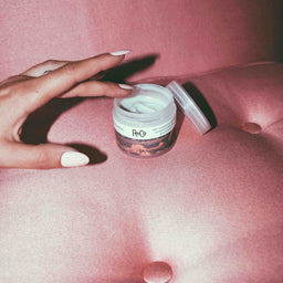 a tub of R+Co Badlands Dry Shampoo Paste being used on a pink couch