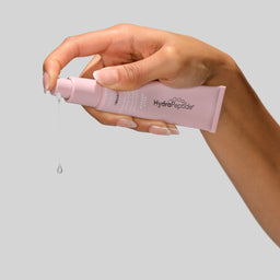 Hand holding a pink skincare product with a gray background