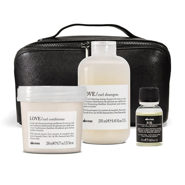 A set of four dvines haircare products arranged in front of a black zippered case on a white background. The set includes LOVE curl shampoo, LOVE curl conditioner, a small bottle of oil, and a black textured carrying case.