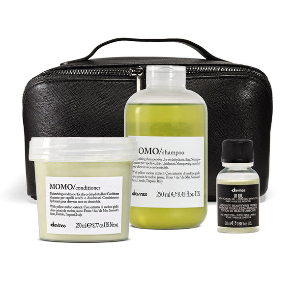 A set of three Davines haircare products arranged in front of a black zippered case on a white background: a large bottle of OMO shampoo, a tub of MOMO conditioner, and a small bottle of Davines Oil Oil.