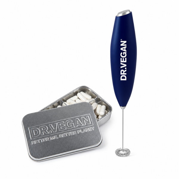A Dr. Vegan milk frother with a navy blue handle and silver metal whisk head, shown next to an open silver metal tin filled with white capsules.